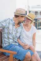 Young hip couple sitting on bench smiling at each other