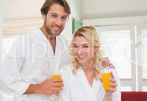 Cute couple in bathrobes smiling at camera together having break