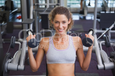 Fit smiling woman using the weights machine for her arms