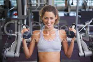 Fit smiling woman using the weights machine for her arms