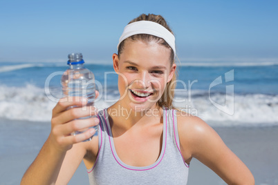 Sporty smiling blonde showing water bottle on the beach