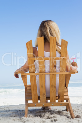 Pretty blonde sitting in deck chair holding coconut drink