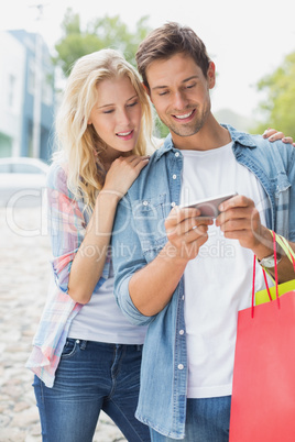 Hip young couple looking at smartphone on shopping trip