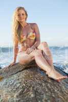 Gorgeous blonde in floral bikini sitting on a rock at beach