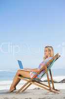 Pretty blonde sitting on beach using her laptop