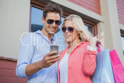 Stylish young couple looking at smartphone holding shopping bags