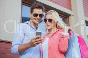 Stylish young couple looking at smartphone holding shopping bags