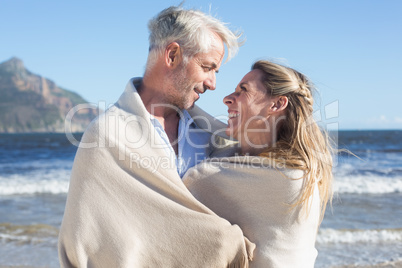 Smiling couple wrapped up in blanket on the beach