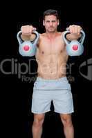 Focused bodybuilder lifting up kettlebells looking at camera