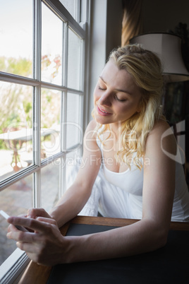 Pretty blonde sitting by the window sending a text