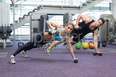 Bodybuilding man and woman holding dumbbells in plank position