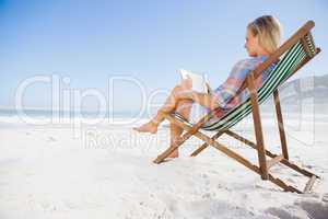 Woman sitting on beach in deck chair using tablet pc