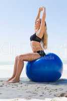 Fit blonde sitting on exercise ball at the beach