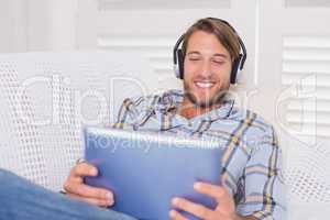 Handsome man lying on couch listening to music on tablet pc