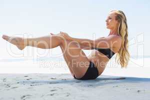 Fit blonde in core balance pilates pose on the beach