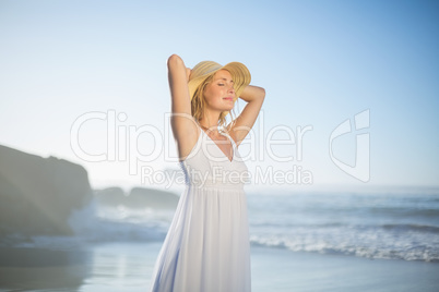 Smiling blonde standing at the beach in white sundress and sunha