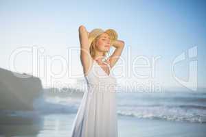 Smiling blonde standing at the beach in white sundress and sunha