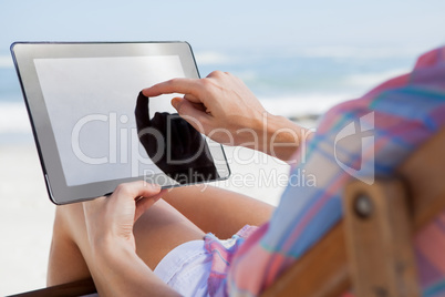 Woman sitting on beach in deck chair using tablet pc