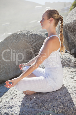 Blonde woman sitting in lotus pose on a rock