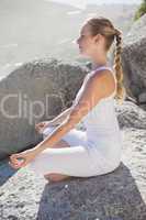 Blonde woman sitting in lotus pose on a rock