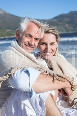 Smiling couple sitting on the beach under blanket