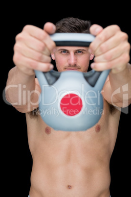 Focused bodybuilder lifting up kettlebell looking at camera