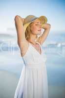 Smiling blonde standing at the beach in white sundress and sunha