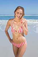 Blonde fit woman in striped bikini at beach smiling at camera