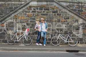 Hip young couple standing by brick wall with their bikes