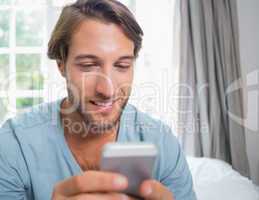 Handsome man sitting on bed sending a text message