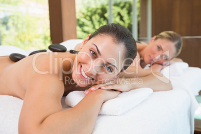 Calm friends lying on massage tables with hot stones on their ba