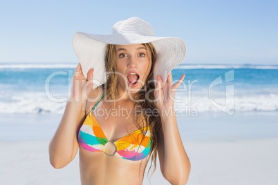 Beautiful girl in bikini and straw hat looking at camera on beac