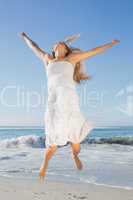 Beautiful blonde in white sundress jumping up on the beach