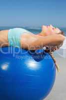 Fit woman lying on exercise ball at the beach stretching