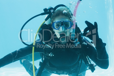 Woman on scuba training submerged in swimming pool making ok sig
