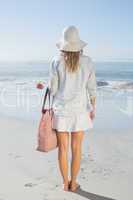 Blonde woman in sunhat carrying beach bag looking out to sea
