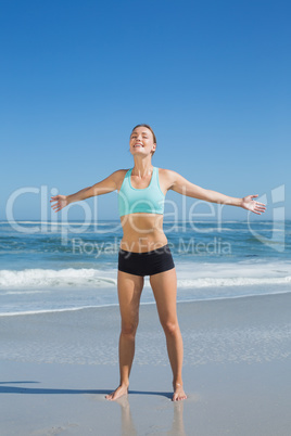 Fit woman standing on the beach with arms out