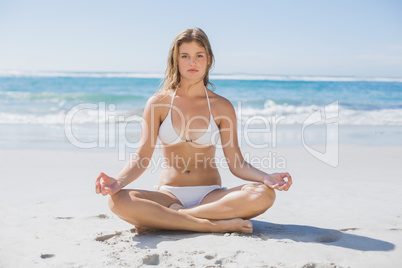 Beautiful girl in white bikini sitting in lotus pose on beach