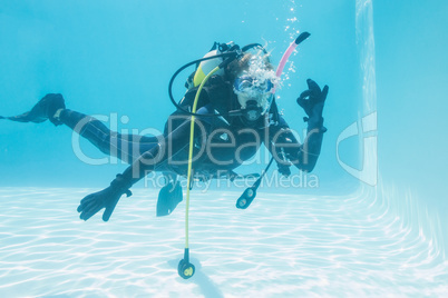 Woman on scuba training submerged in swimming pool making ok sig
