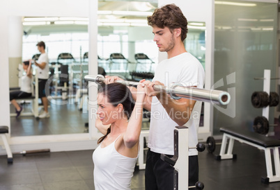 Fit woman lifting barbell with her trainer spotting