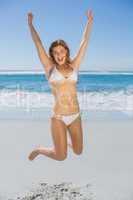 Fit smiling woman in white bikini leaping on beach