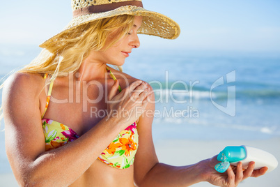Gorgeous blonde in bikini applying suncream on the beach