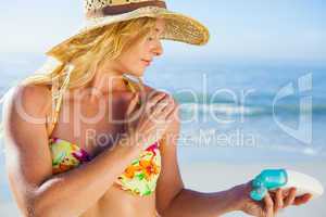 Gorgeous blonde in bikini applying suncream on the beach