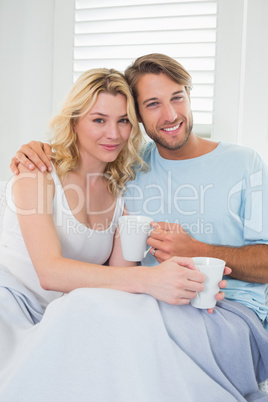 Smiling casual couple sitting on couch having coffee