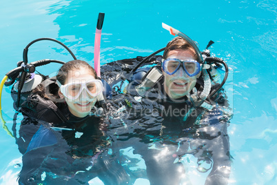 Smiling couple on scuba training in swimming pool looking at cam