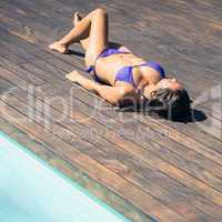 Slim brunette in purple bikini lying poolside