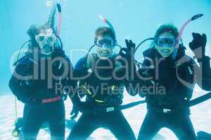 Friends on scuba training submerged in swimming pool making ok s