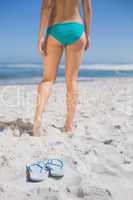 Rear view of fit woman in bikini on beach with flip flops on san