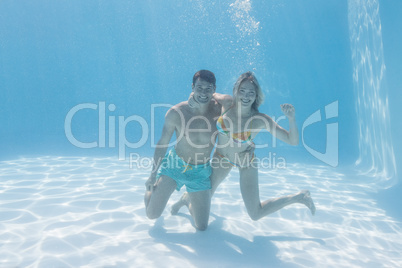 Cute couple smiling at camera underwater in the swimming pool
