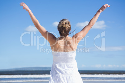Pretty blonde standing with arms outstretched on the beach